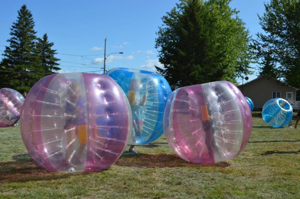 Des participants jouent au soccer-bulle dans de grandes bulles gonflables roses et bleues sur une pelouse.