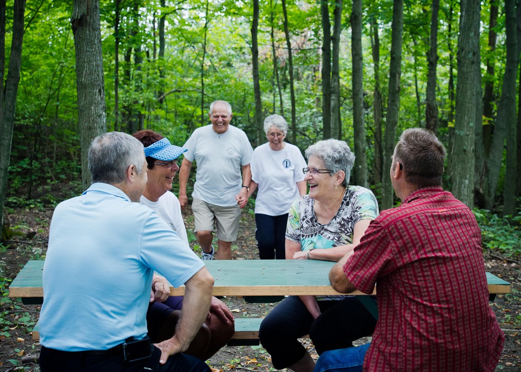 Des aînés souriants se rassemblent autour d’une table de pique-nique dans un sentier boisé.
